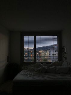 an unmade bed sitting in front of a window with blinds on the windowsill