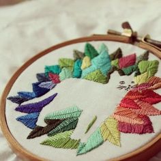 a close up of a embroidery on a white cloth with a wooden hoop holding a needle