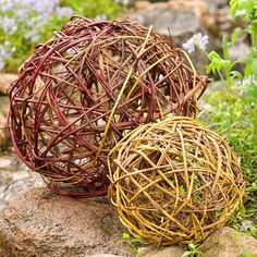 two wicker balls sitting on top of rocks in the grass next to some flowers