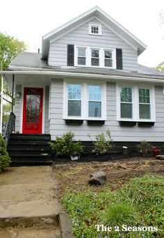 a gray house with red door and steps leading up to the front door is shown