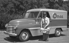 an old black and white photo of a man standing in front of a truck