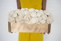 a woman holding a wooden box filled with white flowers on top of a yellow dress