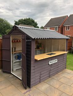 a small outdoor kitchen with an open door on the side of a house in front of a fence