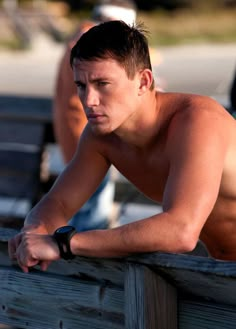 a shirtless man leaning on a wooden bench with his arm resting on the rail