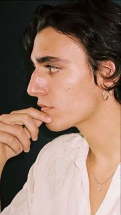 a close up of a person wearing a white shirt and holding his hand to his chin