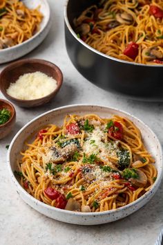 two bowls filled with pasta and sauce on top of a white marble counter next to other dishes