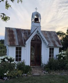 an old white church with a bell tower and flowers in the foreground at sunset