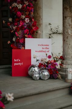 a welcome to the wedding of two people with red flowers and silver balls on steps