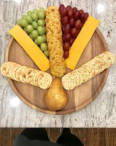 a wooden plate topped with cheese, crackers and grapes