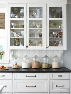 a kitchen with white cabinets and black counter tops, filled with glassware on top