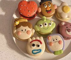 a white plate topped with cupcakes covered in frosting and cartoon characters on top of each other