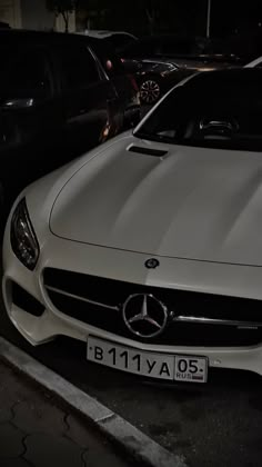 a white car parked next to other cars in a parking lot at night with its hood up