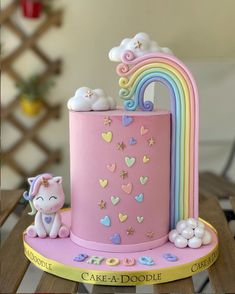 a pink cake decorated with rainbows and clouds