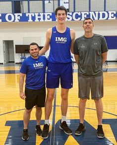 three men standing on a basketball court posing for a photo with one man holding the ball