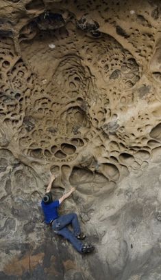 a man climbing up the side of a cliff with his arms in the air while wearing blue