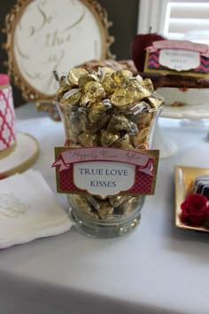 a table topped with a glass vase filled with lots of gold foiled candies