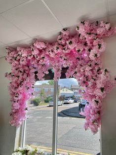 pink flowers hanging from the side of a window in front of a street and buildings