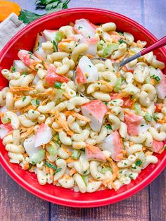 a red bowl filled with macaroni salad next to carrots and parsley