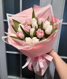 someone holding a bouquet of pink and white tulips in front of a door