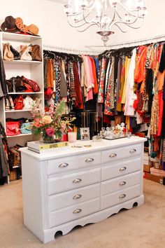 a white dresser sitting in front of a closet filled with clothes