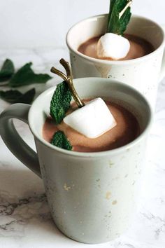 two mugs filled with hot chocolate and marshmallows on a marble table