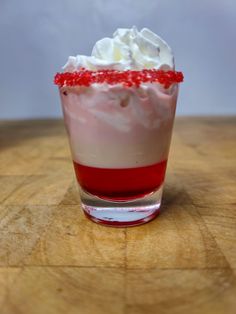 a dessert with whipped cream and red sprinkles in a glass on a wooden table