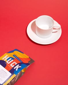 a cup and saucer sitting on top of a red table next to a magazine