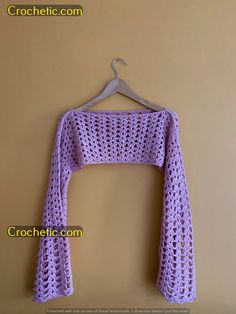 a crocheted sweater hanging on a hanger next to a wall with the words crochet com written below it