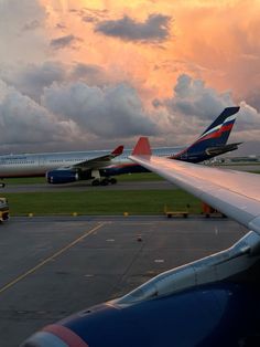 two airplanes are parked on the runway at an airport as the sun sets behind them