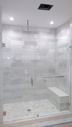 a walk in shower sitting next to a white tiled wall and floor with a glass door