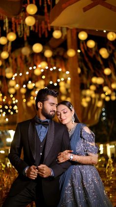 a man and woman dressed in formal wear posing for a photo with lights hanging from the ceiling behind them