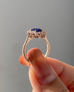 a hand holding a ring with three stones on it's sides and the middle stone is blue