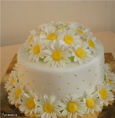 a white cake with yellow and white daisies on the top is sitting on a table