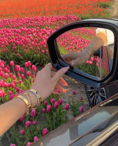 a woman's hand on the side mirror of a car in front of a field of tulips