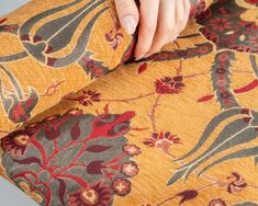 a woman's hand on the back of a yellow floral patterned chair with red and green flowers