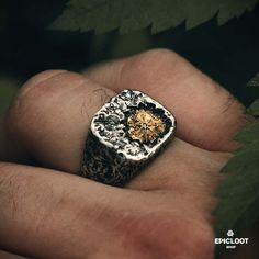 a man's hand holding a silver and gold ring with an intricate design on it