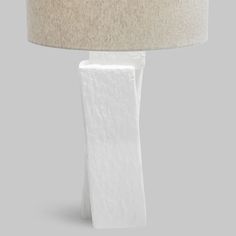 a white table lamp sitting on top of a floor next to a lampshade