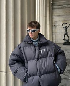 a young man wearing sunglasses standing in front of columns