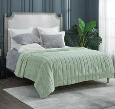 a bed with green comforter and pillows next to a potted plant on a rug