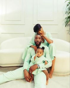 a man and woman sitting on top of a couch holding a baby