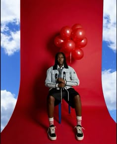 a man sitting in front of a red backdrop with balloons