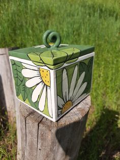 a green and white box sitting on top of a tree stump in the grass with flowers painted on it