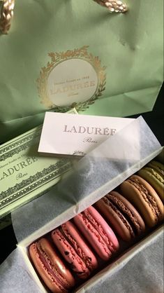 a box filled with different colored macaroons next to money