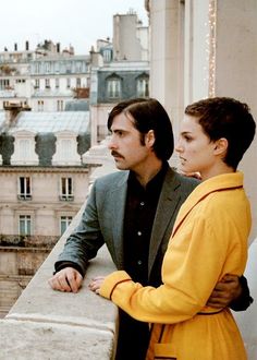 a man and woman standing next to each other on top of a building with buildings in the background