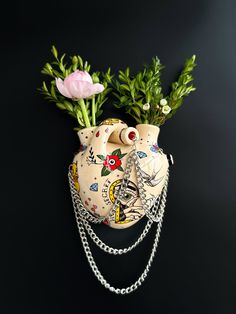 two small vases with flowers and chains attached to them on a black surface next to a pink flower