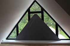 a triangle shaped window in the corner of a room with wood flooring and white walls