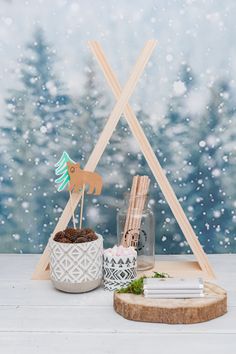 a wooden teepee and some plants in a pot on a table with snowflakes