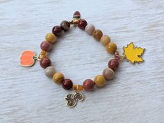 This beaded stretch charm bracelet features 4 enamel fall themed charms: 1/2 inch brown squirrel charm, 1 inch leaf charm, 1/2 inch acorn charm, 3/4 inch pumpkin Charm, along with 8mm mookaite round beads, 4mm faceted yellow/brown glass seed beads, and has a total measurement of 7 inches around. Brown Squirrel, Themed Jewelry, Bracelets Handmade Beaded, Leaf Charms, Cute Bracelets, Glass Seed Beads, Autumn Outfit, Blue Earrings, Autumn Theme