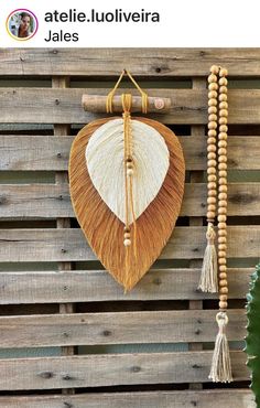 a wooden wall hanging with tassels attached to it's sides and an oval shaped shell hanging from the side