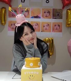 a woman sitting at a table with a cake in front of her and balloons behind her